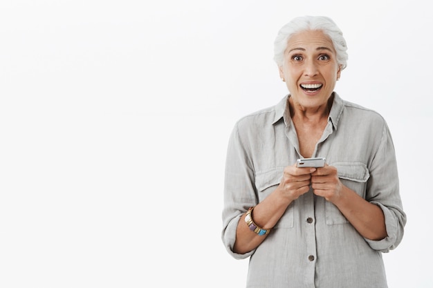 Free photo excited and amazed granny holding mobile phone and smiling happy