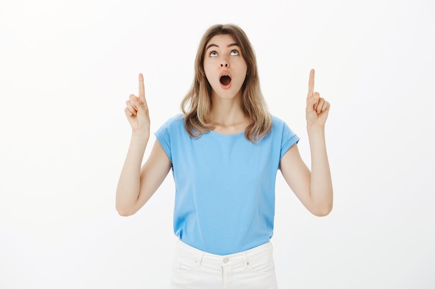 Free Photo excited and amused blond woman open mouth wondered, pointing fingers up