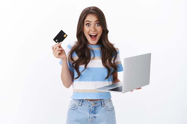 Excited amused good-looking female hold laptop and credit card, smiling fascinated, ready pay for purchase, browsing internet buying gadgets online, adore how easy shopping with her bank