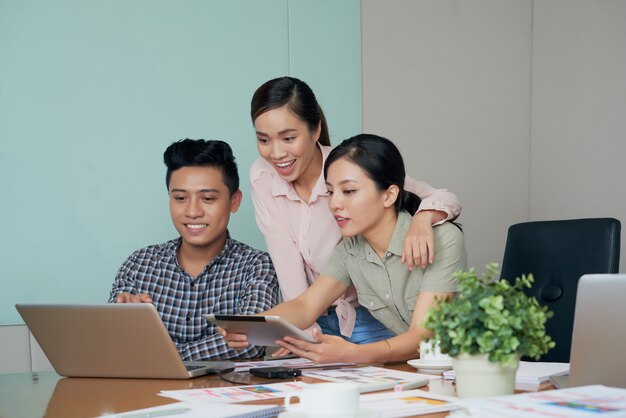 Excited Asian colleagues looking at laptop screen together in office