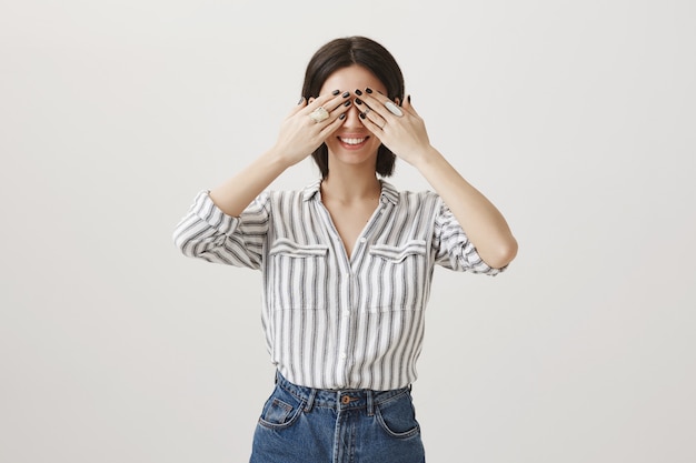 Excited attractive woman awaiting for surprise with closed eyes and happy smile