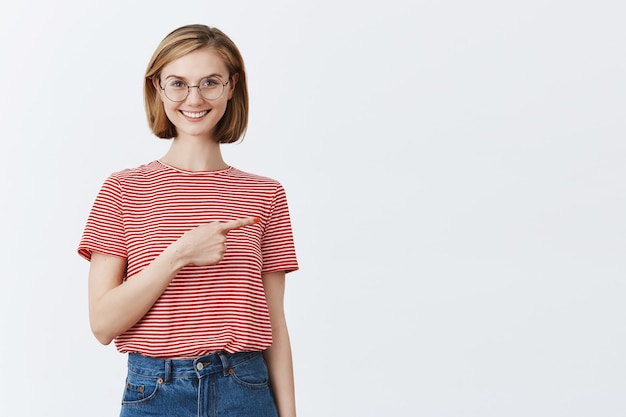 Free photo excited attractive young girl in glasses showing way, pointing finger right at copyspace