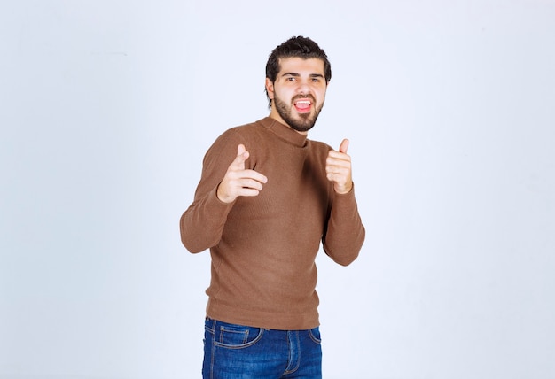 Excited bearded man in brown sweater pointing fingers at camera isolated on a white background. High quality photo