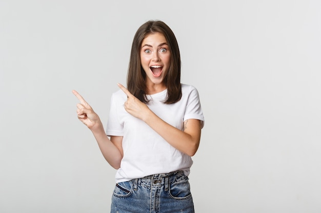 Excited beautiful girl smiling, pointing fingers upper left corner and looking pleased at logo.