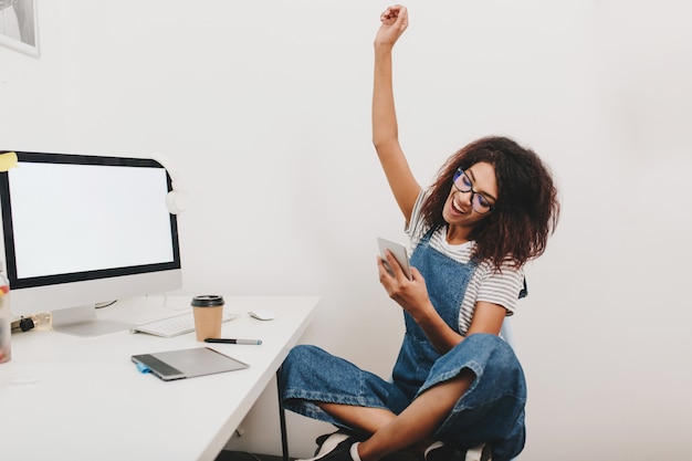 Excited black girl sitting with legs crossed and happy laughing, reading phone message