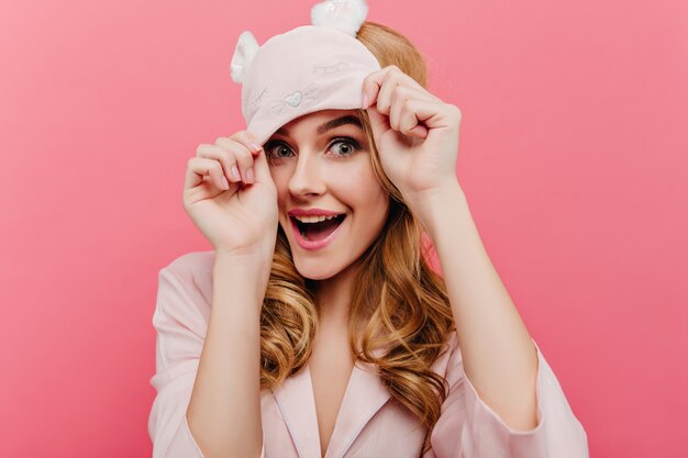 Excited blonde woman with blue eyes and laughing. Indoor close-up portrait of lovely lady in eyemask expressing happiness.