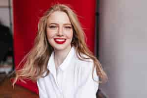 Free photo excited blonde woman with red lips laughing at camera studio shot of cute girl in white shirt