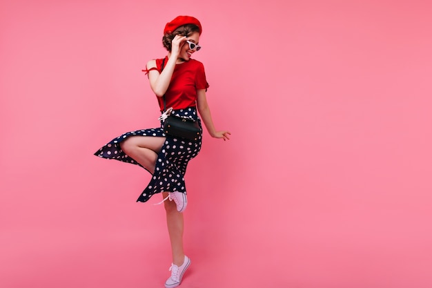 Free photo excited brunette lady in black skirt dancing on rosy wall. appealing white girl in french beret jumping.