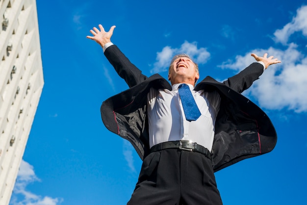 Free photo excited businessman raising his arms against sky