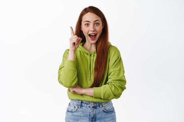 Excited and creative girl student, ginger female model suggest a plan, raise finger eureka sign, pitching an idea, have great solution, standing against white background