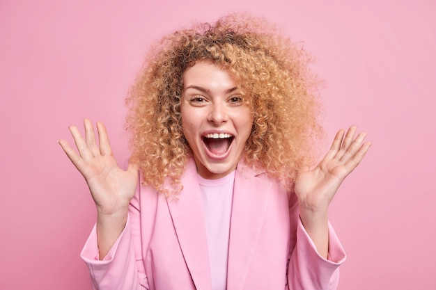 Free photo excited curly haired european woman raises palms exclaims loudly keeps mouth opened reacts on awesome news