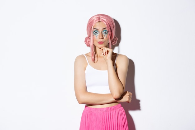 Free photo excited cute party girl with pink wig and halloween makeup, looking with interest at camera, listening to something, standing.