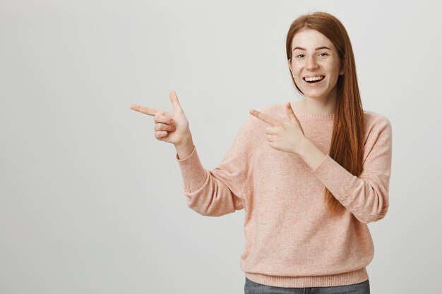 Excited cute redhead teenage girl pointing fingers left