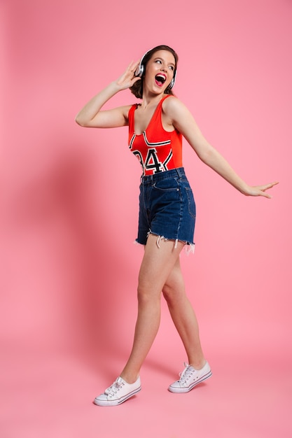 Excited emotional young lady dancing isolated pink 