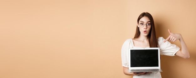 Free Photo excited girl in glasses making presentation on computer pointing hand at laptop screen and say wow s