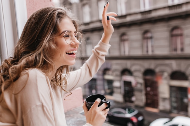 Free photo excited girl with curly hairstyle waving hand to someone, looking at window