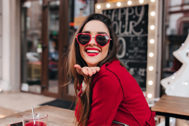 Excited girl with light-brown hair sending air kiss in cafe