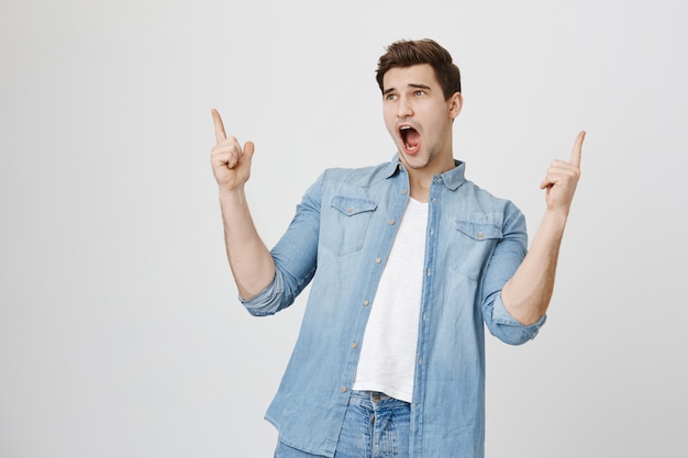 Excited handsome guy pointing fingers up, showing advertisement