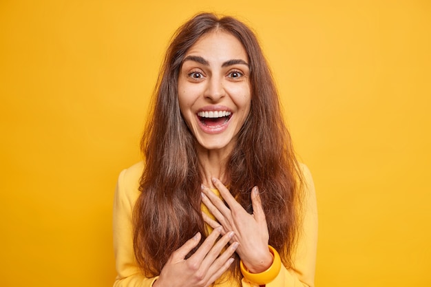 Excited happy European woman with natural long hair smiles broadly hears excellent news