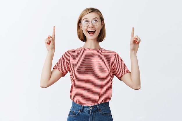 Free Photo excited happy pretty woman in glasses pointing fingers and looking up with amazed smile