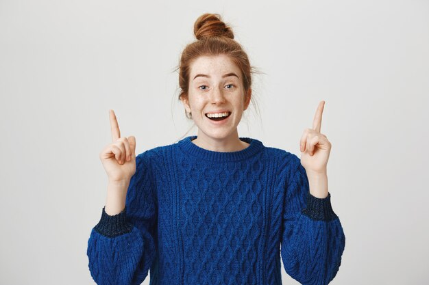 Excited happy redhead woman pointing fingers up