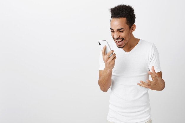 Excited and happy triumphing african american man looking at mobile phone screen with thrilled face, rejoicing