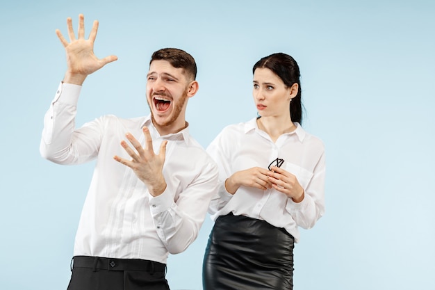 Excited happy young couple looking at camera with delight. Businessman and woman isolated on blue studio background