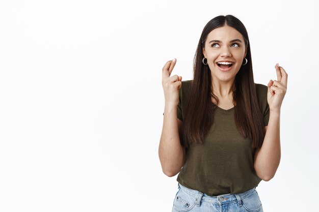 Excited hopeful woman making her wish, cross fingers for good luck, gasping and looking at upper left corner