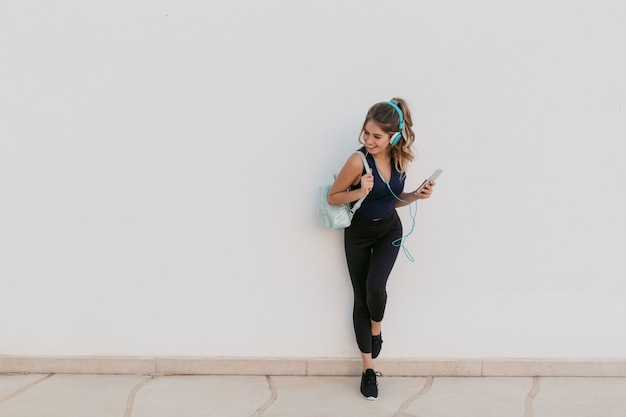 Free photo excited joyful young woman in sportswear listening to music through headphones. smiling to side, expressing positivity, true emotions, healthy lifestyle, fitness.