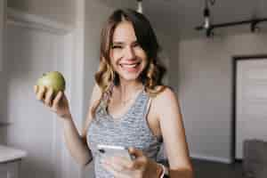 Free photo excited lady in gray clothes posing with apple. amazing blonde woman enjoying fruits in morning.