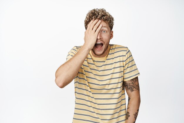 Excited laughing blond man looking surprised and amazed hear great big news reacting to awesome surprise standing over white background