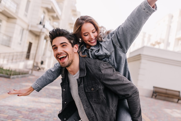 Free photo excited man in black denim jacket chilling with girlfriend. outdoor portrait of happy couple exploring city.