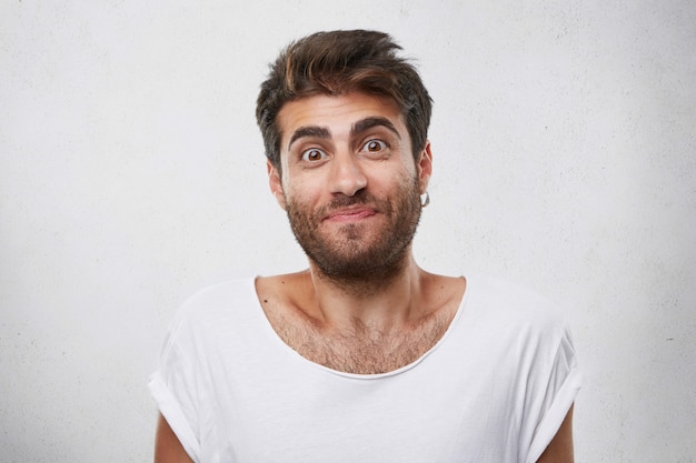 Free photo excited man with thick dark eyebrows and beard being pleasantly surprised looking with wide opened eyes having doubtful look. indoor shot of handsome guy having confused expression