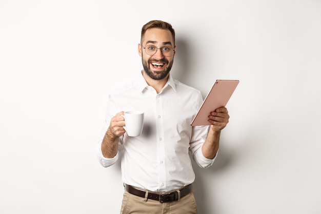 Excited manager reading on digital tablet, working and drinking coffee, standing  