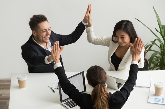 Excited multiracial team holding hands giving high five celebrating success