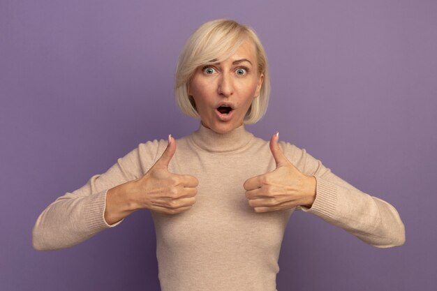 Excited pretty blonde slavic woman thumbs up of two hands on purple