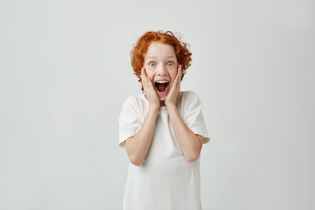 Free photo excited redhead boy with freckles holding face with hands, with happy expression and opened mouth after parents gave him sweets.