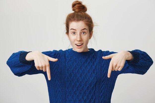 Excited redhead girl pointing fingers down