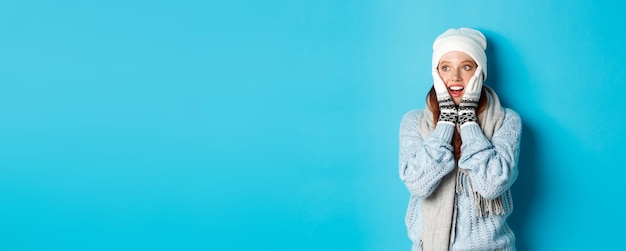 Free photo excited redhead girl staring left at logo wearing winter clothes beanie gloves and sweater standing