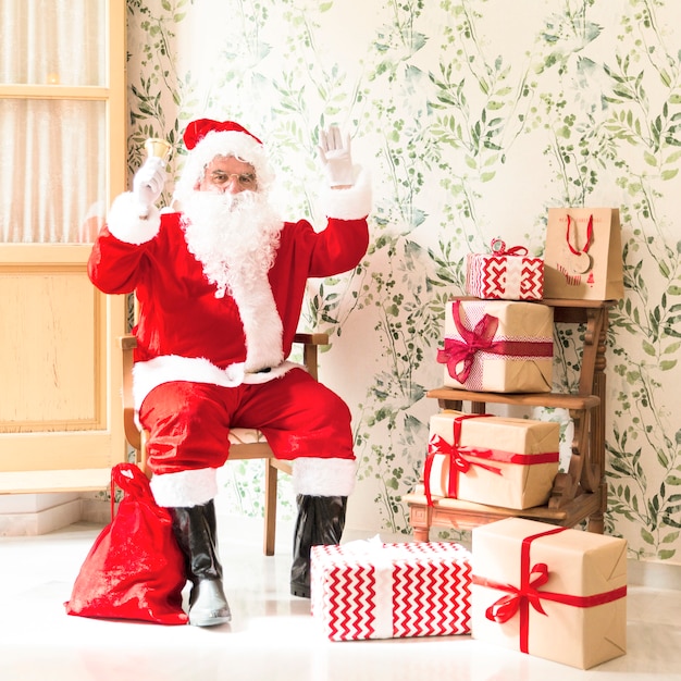 Excited Santa Claus sitting on chair next to presents