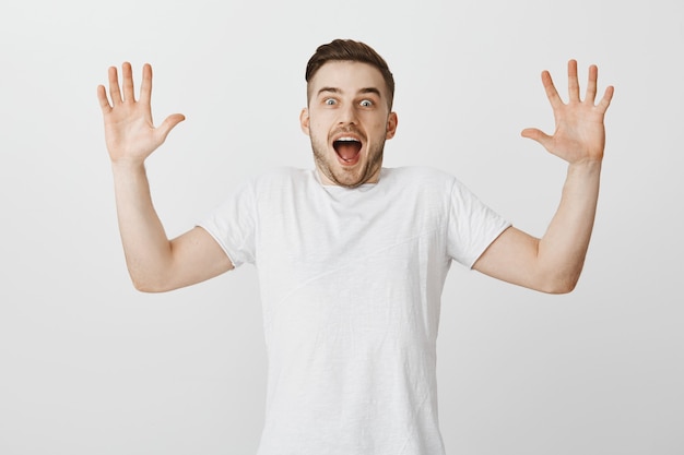 Excited and surprised young guy raising hands up and gasping astounded with big news