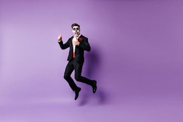 Free photo excited welldressed guy with scary makeup fooling around in studio zombie model funny jumping on purple background