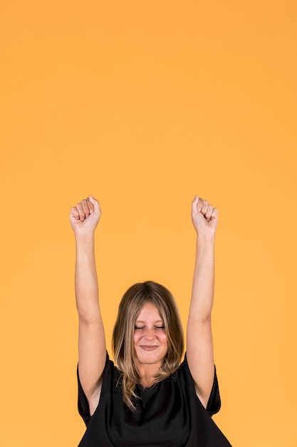 Excited woman pumping fists with his eyes closed over yellow backdrop