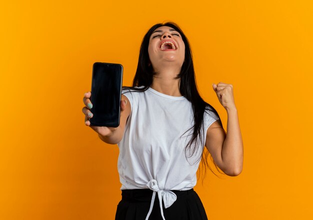 Excited young caucasian woman holds phone and keeps fist looking up