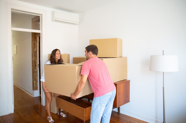 Excited young couple moving into new flat, carrying carton boxes carefully