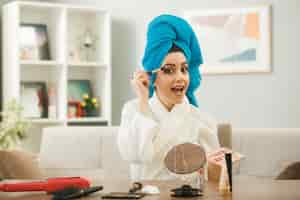 Free photo excited young girl applying eyeshadow with makeup brush sitting at table with makeup tools in living room