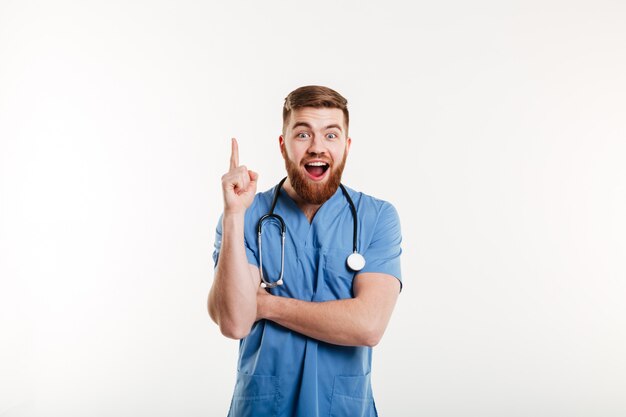 Excited young male doctor pointing finger up at copyspace