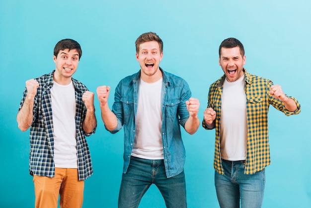 Excited young male friends clenching their fist against blue background