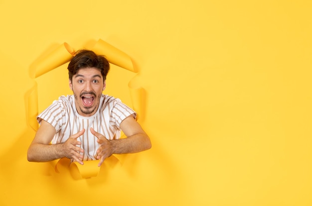 Free photo excited young male standing on torn yellow paper surface