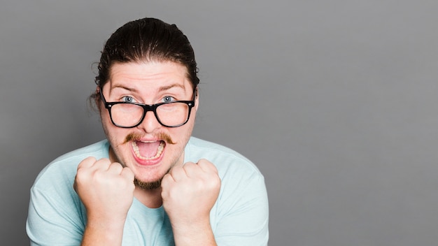 Free Photo excited young man flexing his muscle against grey wall